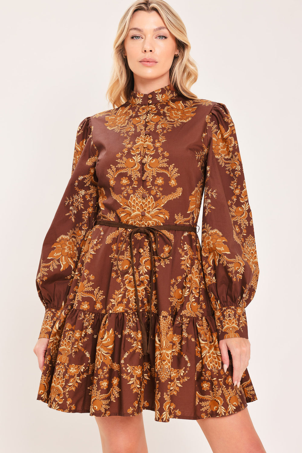A woman modeling a brown and gold damask-patterned long-sleeve mini dress with a high mock neck and a matching waist tie | Flying Tomato