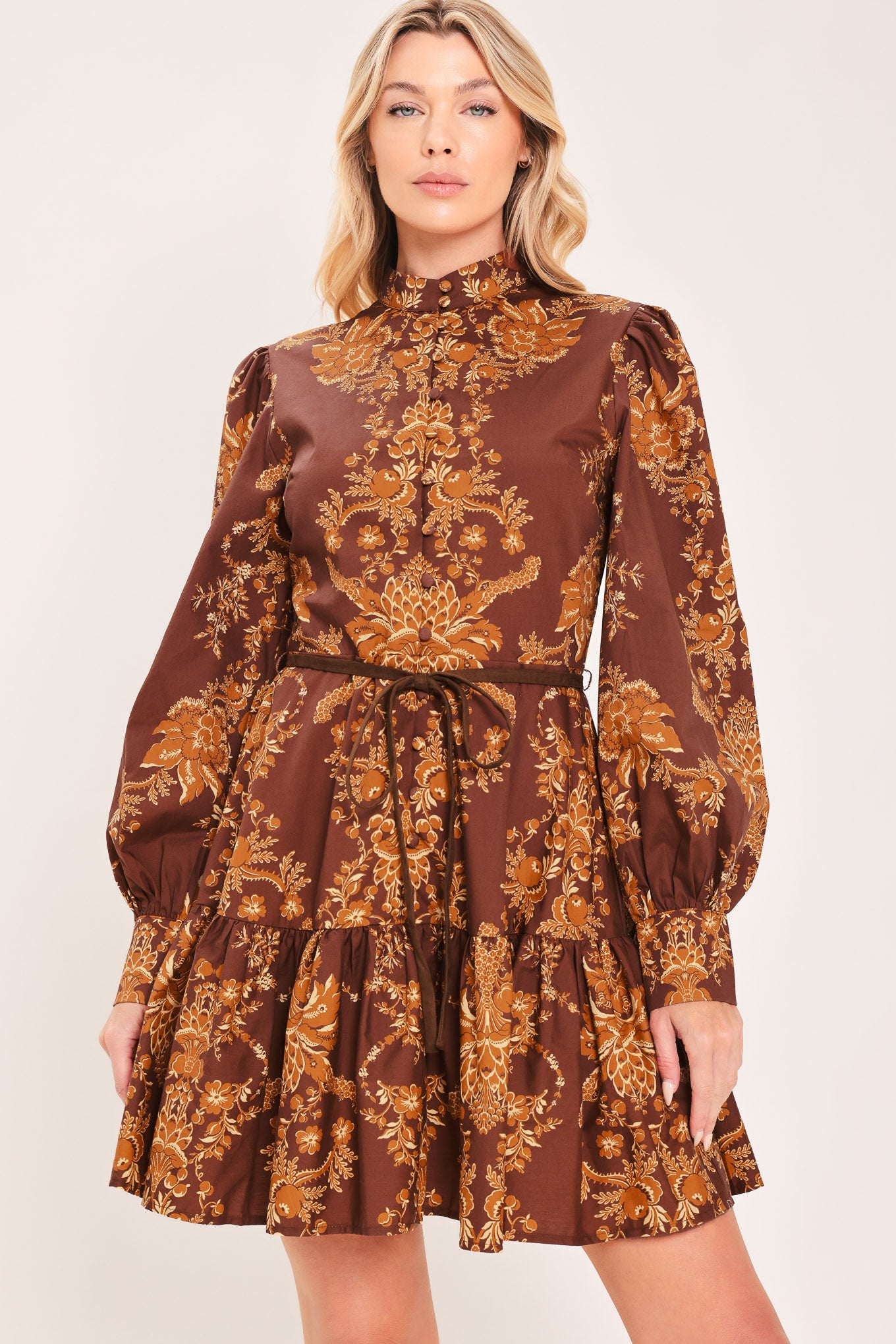 A woman modeling a brown and gold damask-patterned long-sleeve mini dress with a high mock neck and a matching waist tie | Flying Tomato