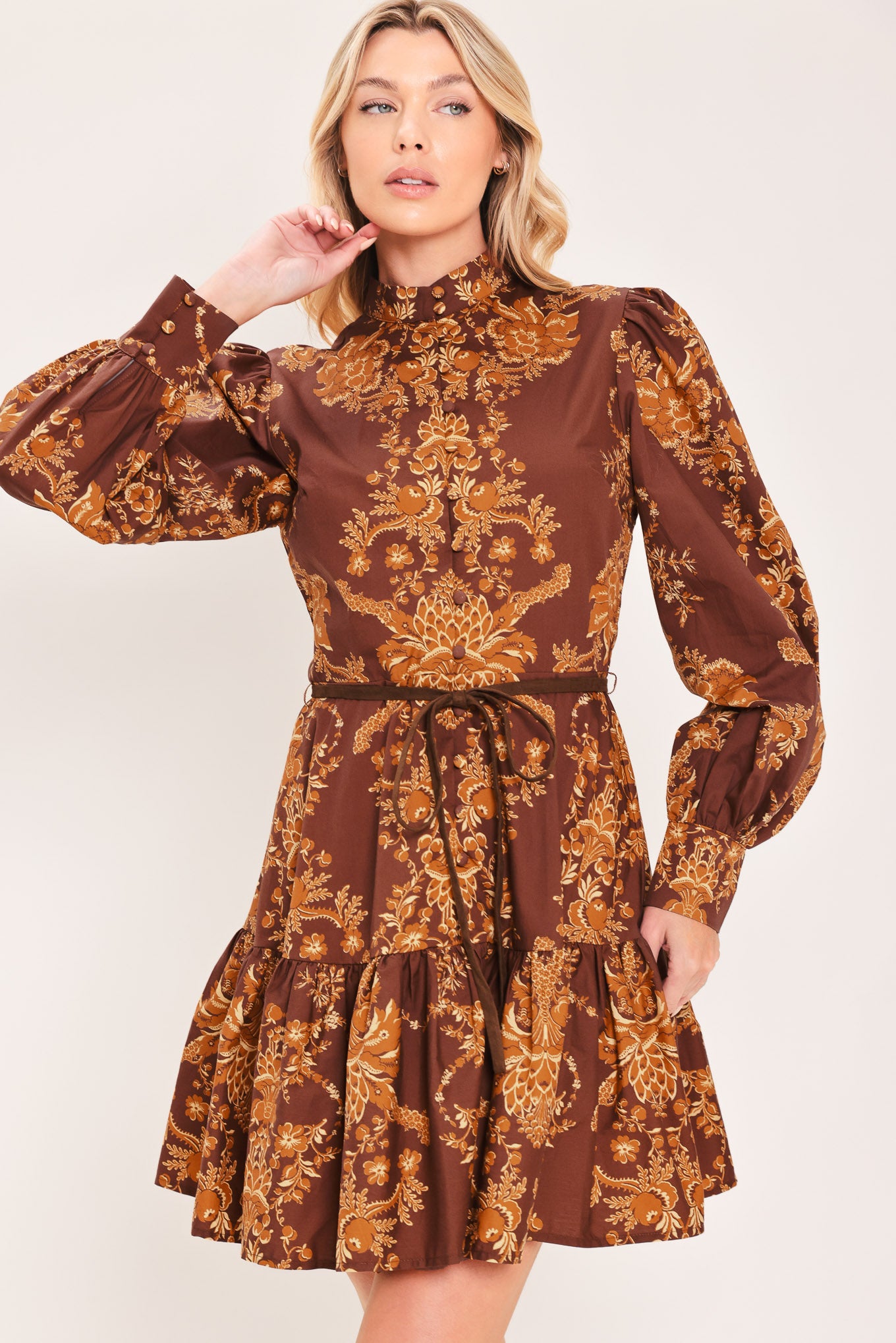 A woman modeling a brown and gold damask-patterned long-sleeve mini dress with a high mock neck and a matching waist tie | Flying Tomato