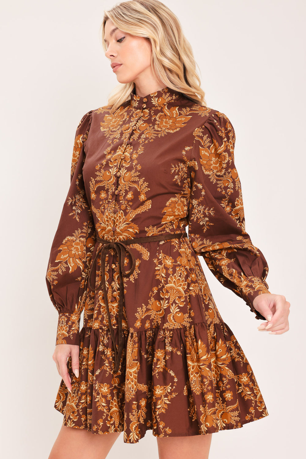 A woman modeling a brown and gold damask-patterned long-sleeve mini dress with a high mock neck and a matching waist tie | Flying Tomato