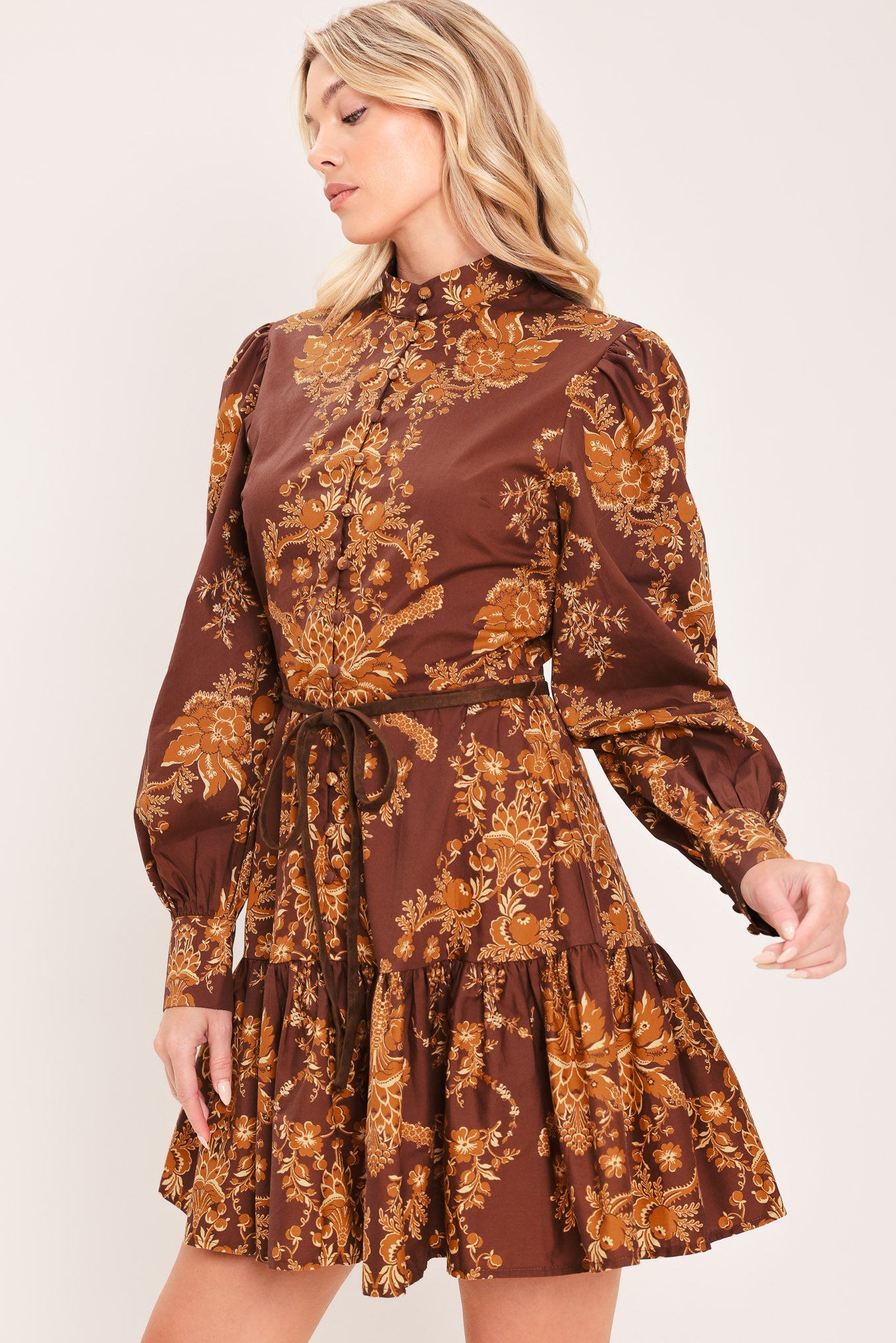 A woman modeling a brown and gold damask-patterned long-sleeve mini dress with a high mock neck and a matching waist tie | Flying Tomato