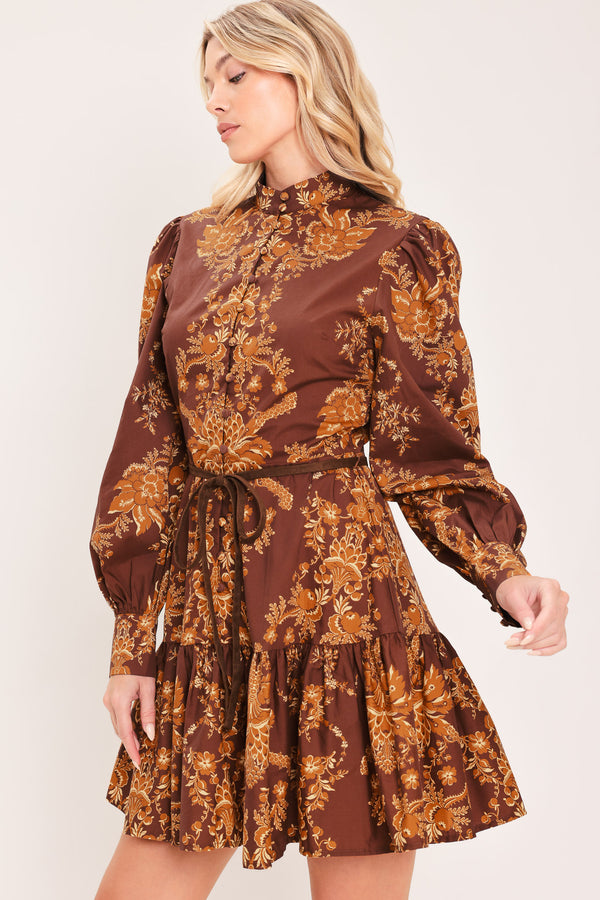A woman modeling a brown and gold damask-patterned long-sleeve mini dress with a high mock neck and a matching waist tie | Flying Tomato