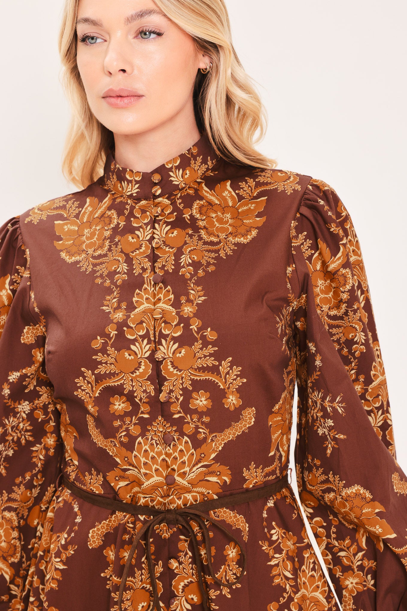 A woman modeling a brown and gold damask-patterned long-sleeve mini dress with a high mock neck and a matching waist tie | Flying Tomato