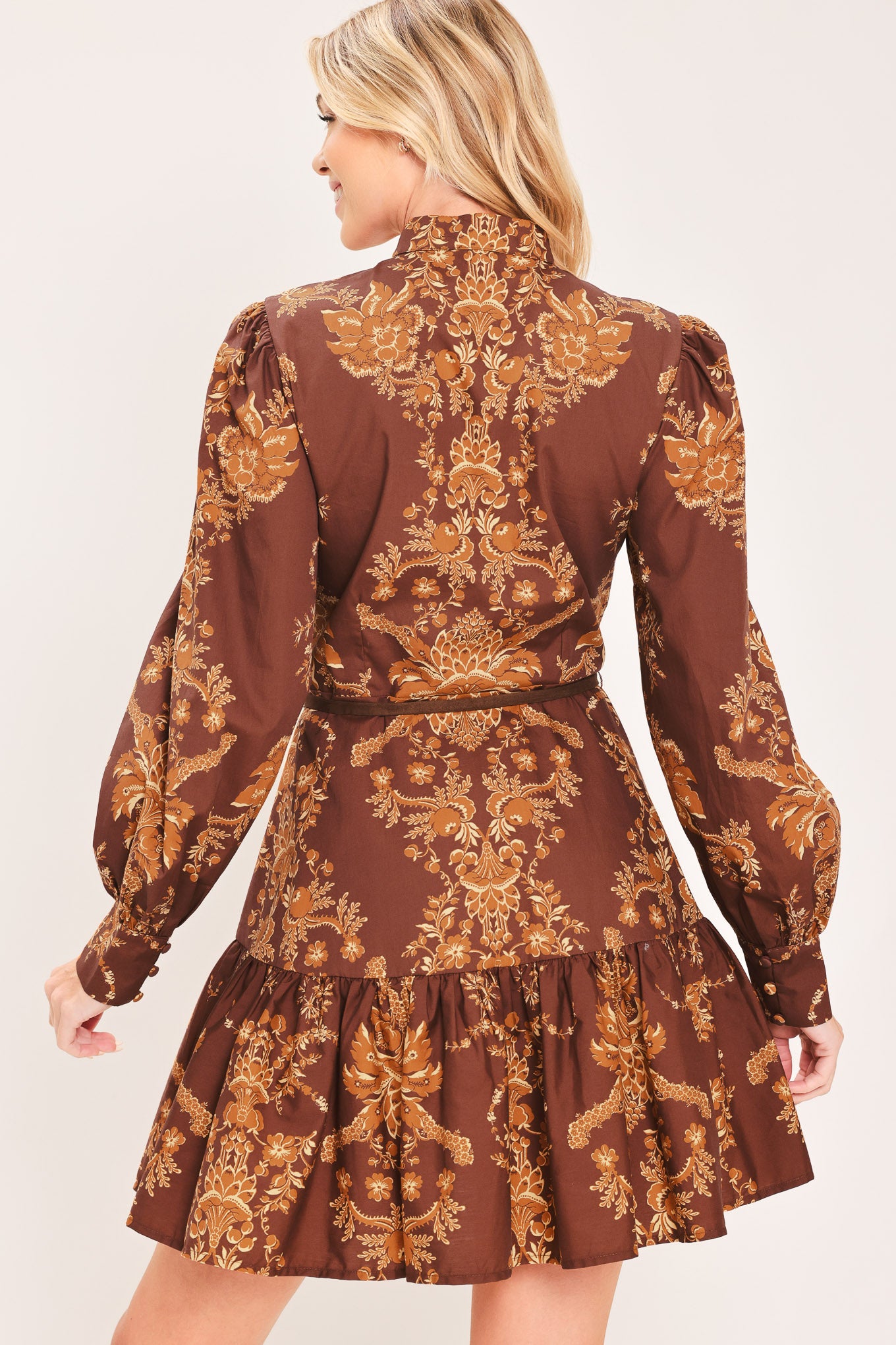 A woman modeling a brown and gold damask-patterned long-sleeve mini dress with a high mock neck and a matching waist tie | Flying Tomato
