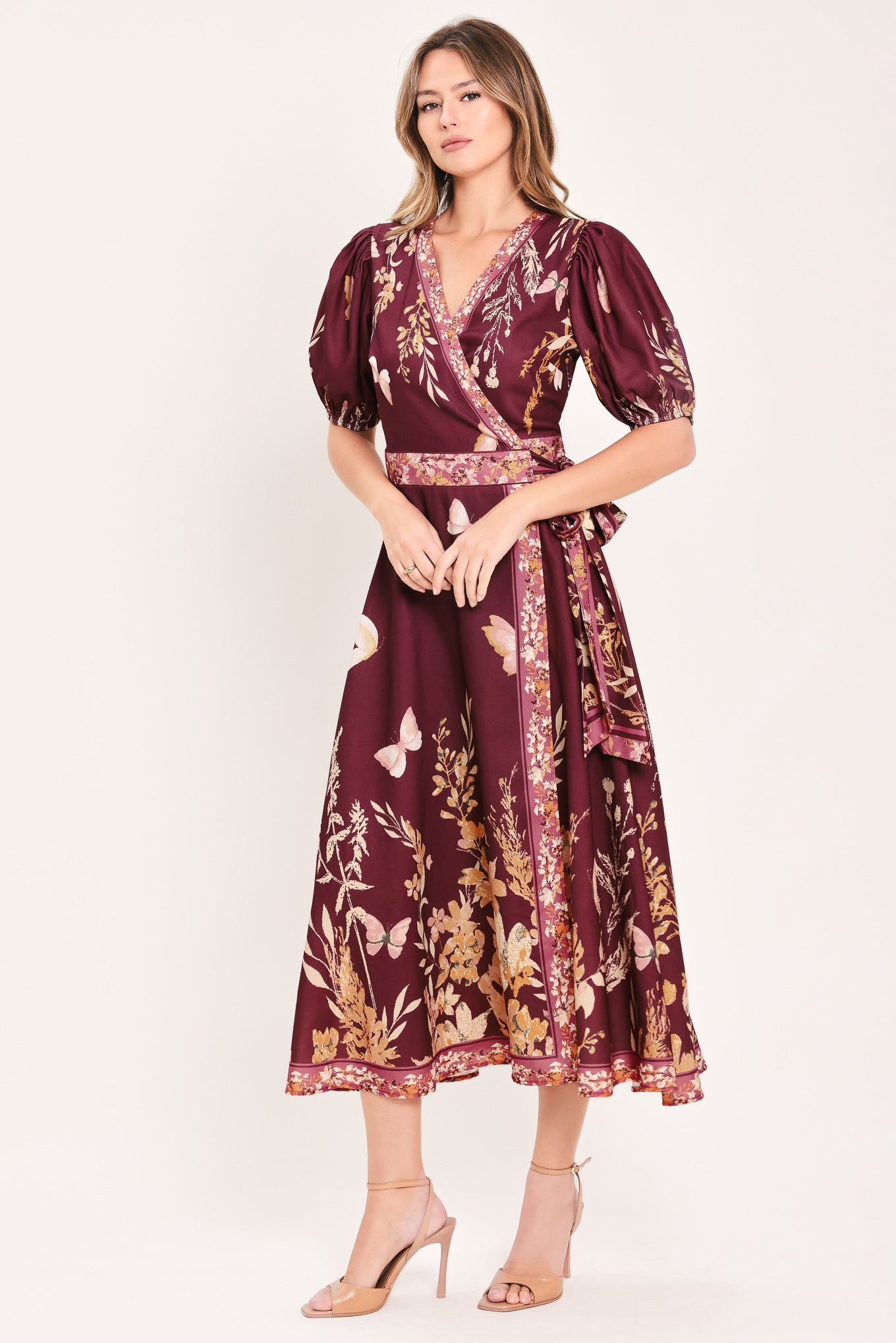 A woman wearing a burgundy midi wrap dress with a floral and butterfly print, featuring puff sleeves, a V-neckline, and a matching waist tie | Flying Tomato