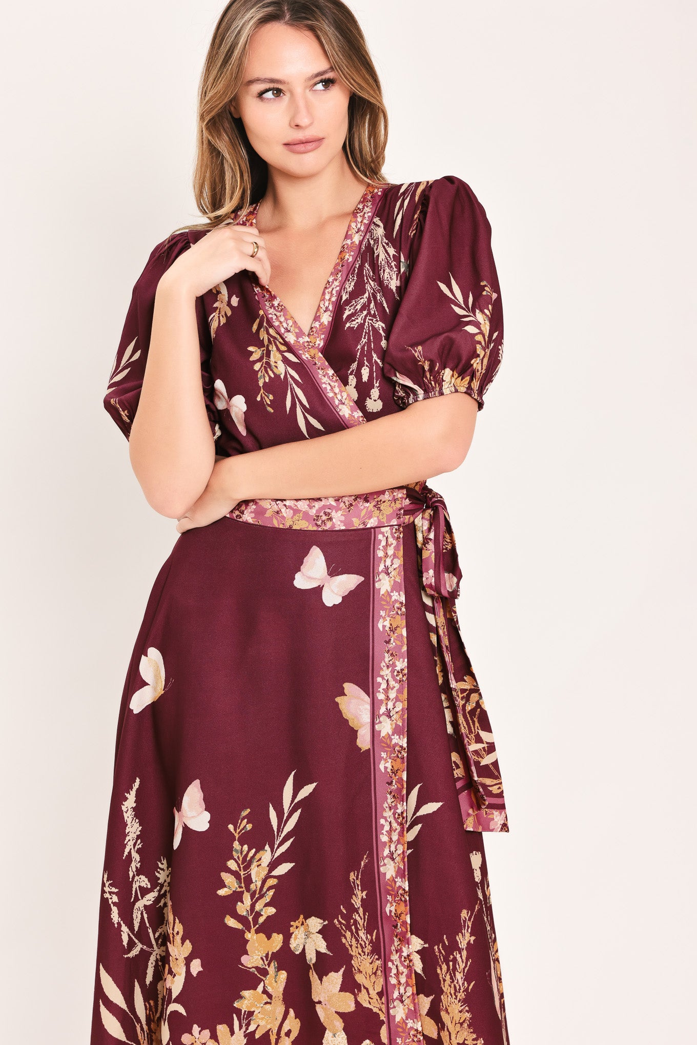 A woman wearing a burgundy midi wrap dress with a floral and butterfly print, featuring puff sleeves, a V-neckline, and a matching waist tie | Flying Tomato