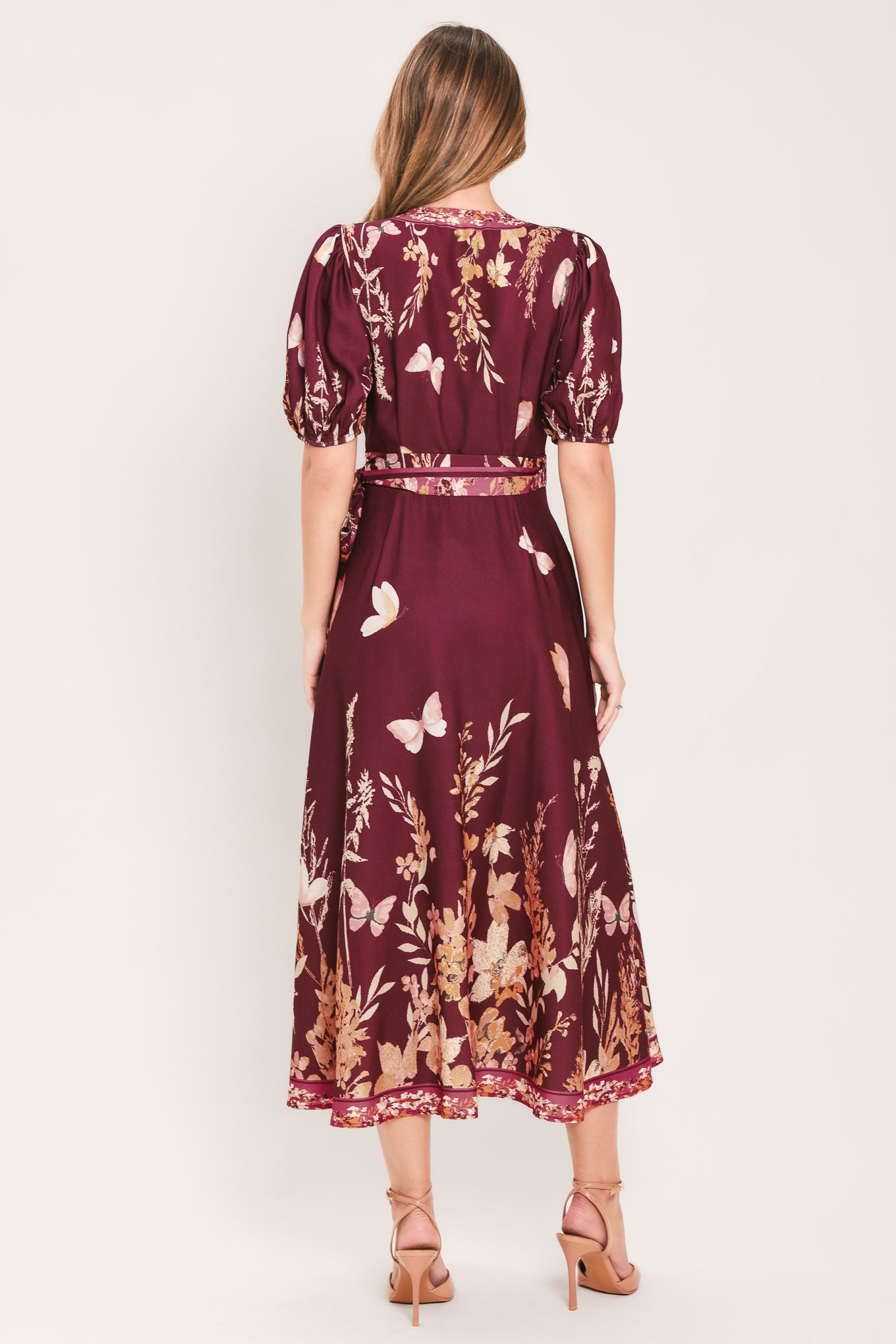 A woman wearing a burgundy midi wrap dress with a floral and butterfly print, featuring puff sleeves, a V-neckline, and a matching waist tie | Flying Tomato