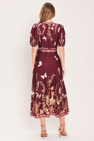 A woman wearing a burgundy midi wrap dress with a floral and butterfly print, featuring puff sleeves, a V-neckline, and a matching waist tie | Flying Tomato