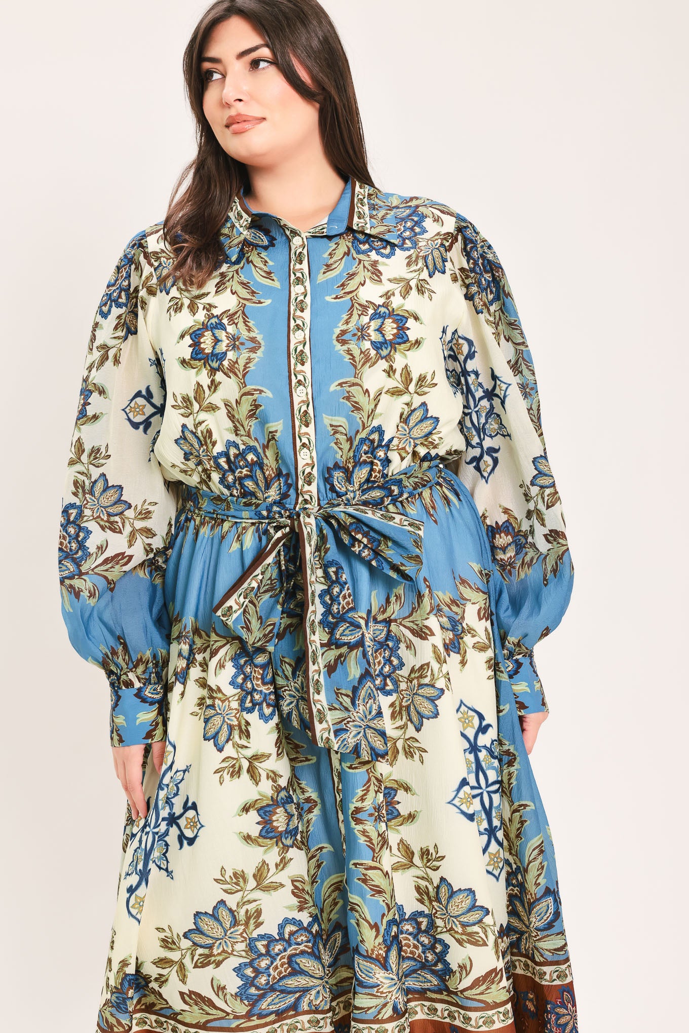 A woman wearing a long-sleeved midi dress with a blue, beige, and brown floral pattern, featuring a tie waist belt | Flying Tomato Curve