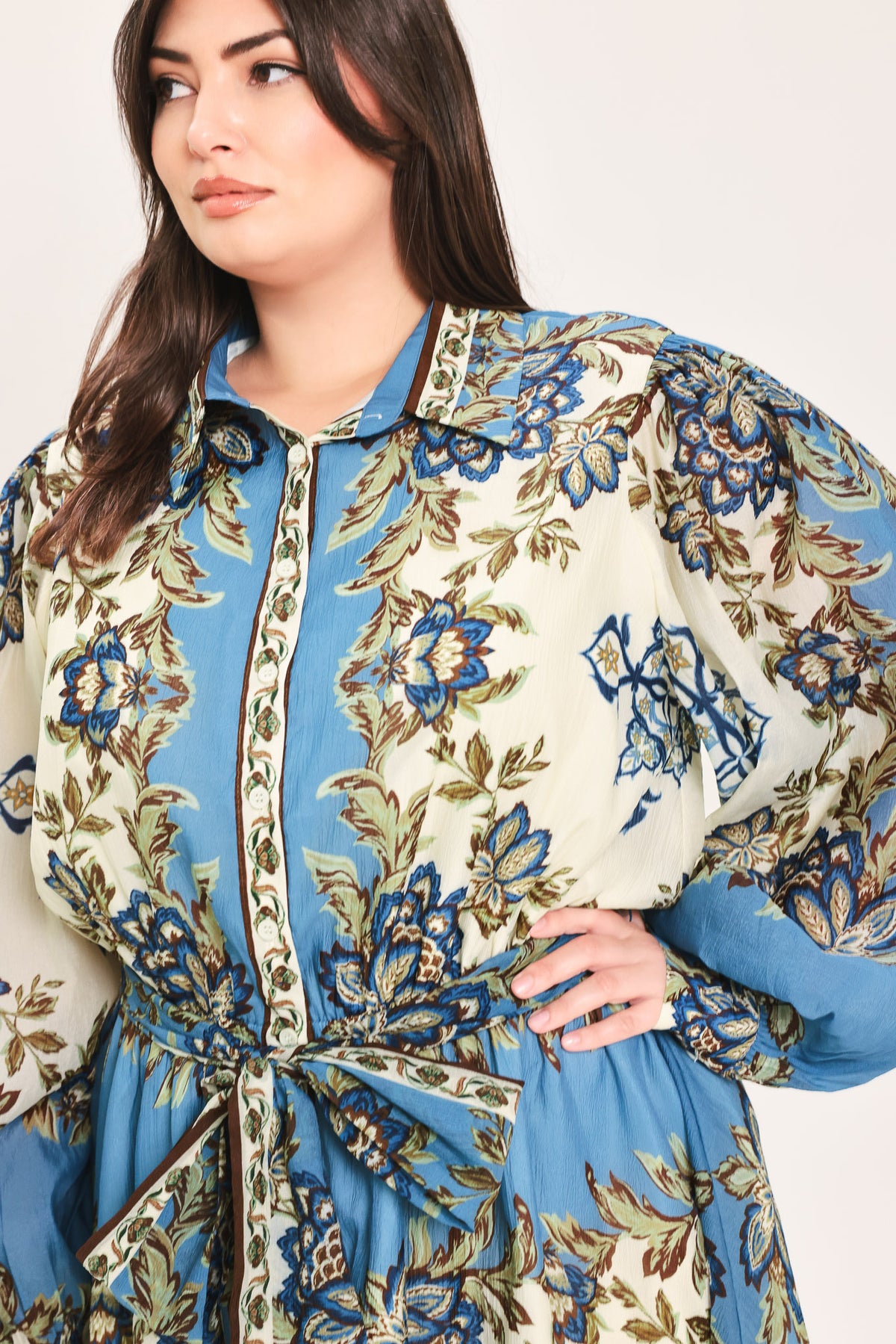 A woman wearing a long-sleeved midi dress with a blue, beige, and brown floral pattern, featuring a tie waist belt | Flying Tomato Curve