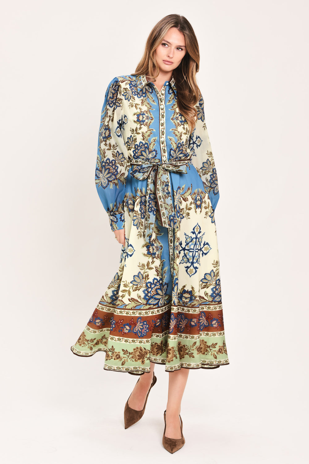 A woman wearing a long-sleeved midi dress with a blue, beige, and brown floral pattern, featuring a tie waist belt | Flying Tomato