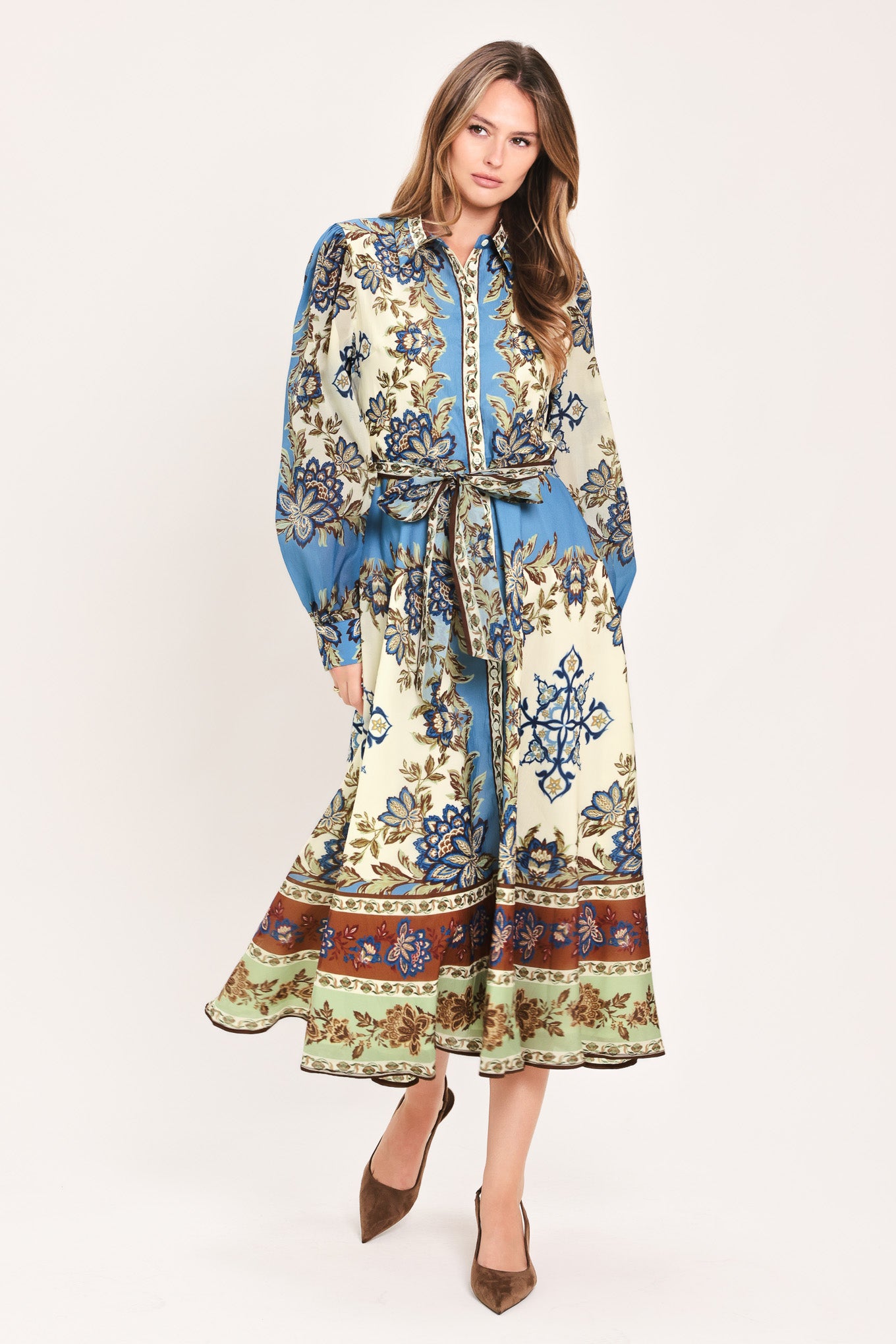 A woman wearing a long-sleeved midi dress with a blue, beige, and brown floral pattern, featuring a tie waist belt | Flying Tomato