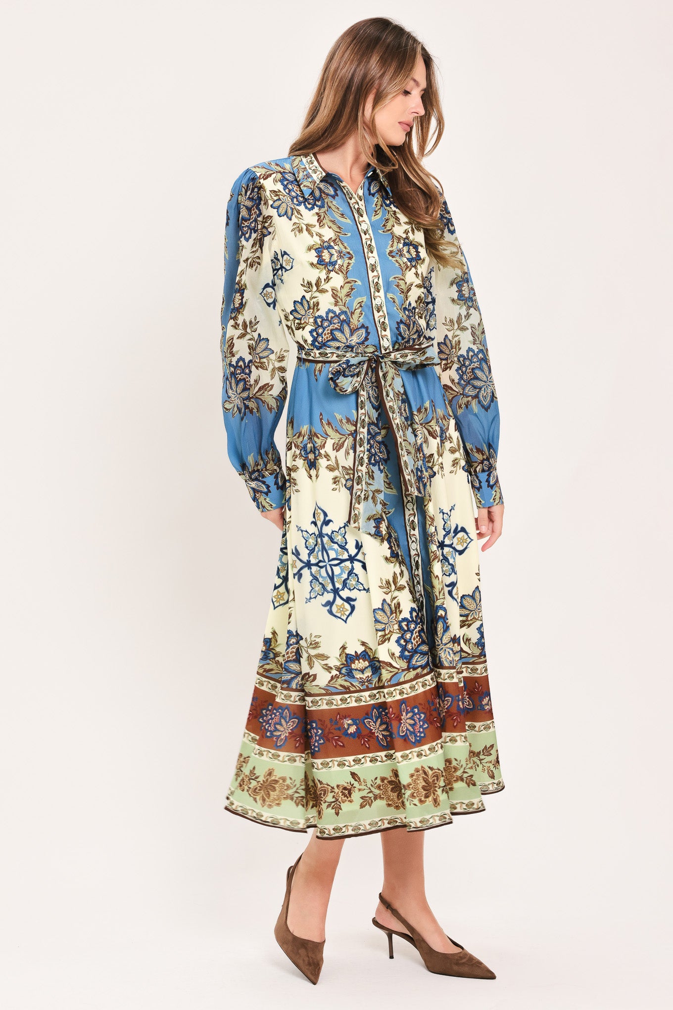 A woman wearing a long-sleeved midi dress with a blue, beige, and brown floral pattern, featuring a tie waist belt | Flying Tomato