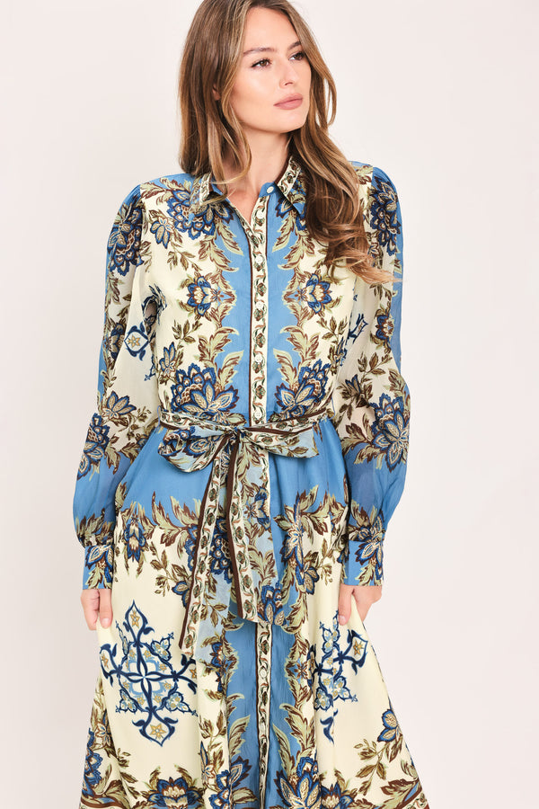 A woman wearing a long-sleeved midi dress with a blue, beige, and brown floral pattern, featuring a tie waist belt | Flying Tomato