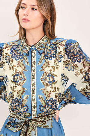 A woman wearing a long-sleeved midi dress with a blue, beige, and brown floral pattern, featuring a tie waist belt | Flying Tomato