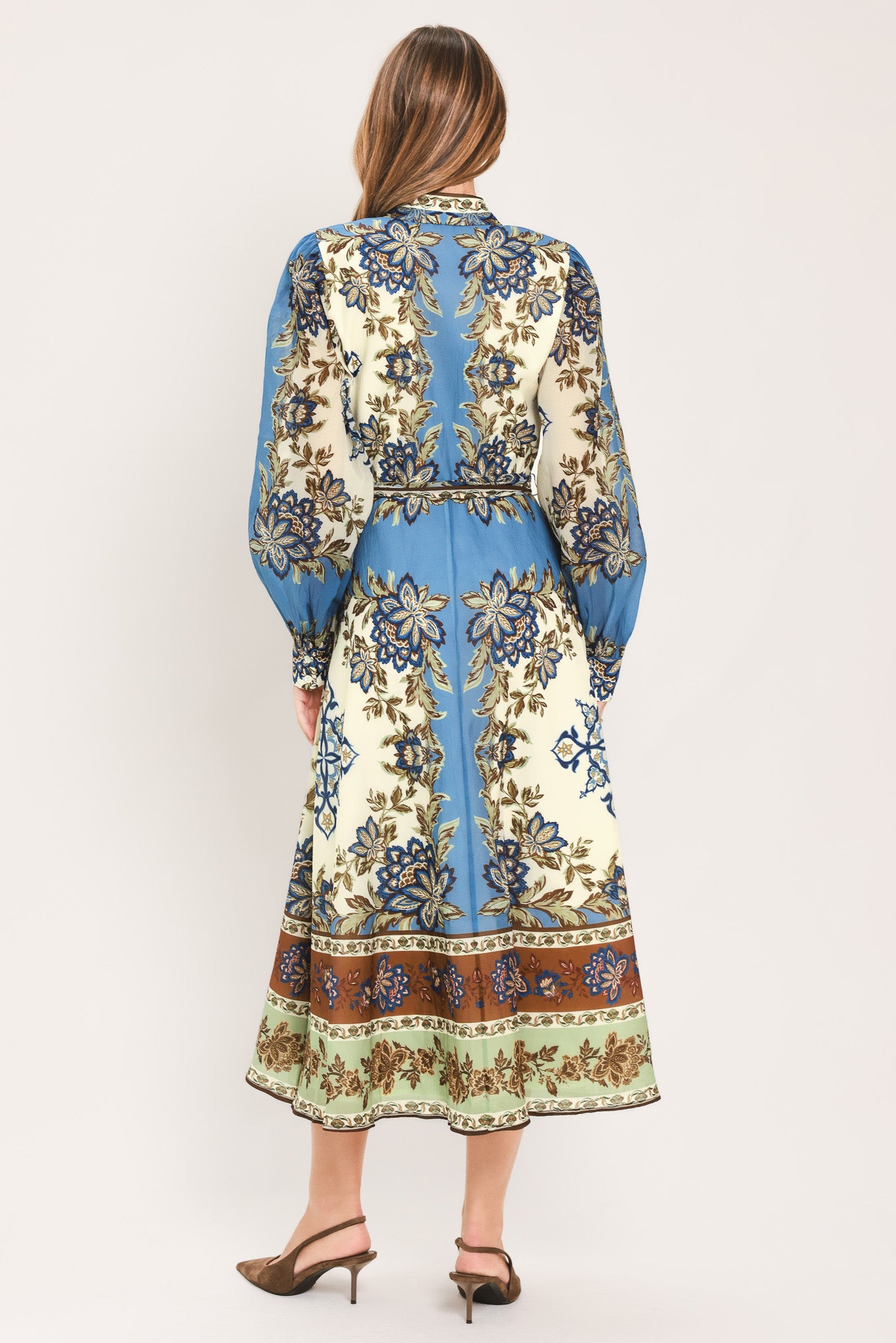 A woman wearing a long-sleeved midi dress with a blue, beige, and brown floral pattern, featuring a tie waist belt | Flying Tomato