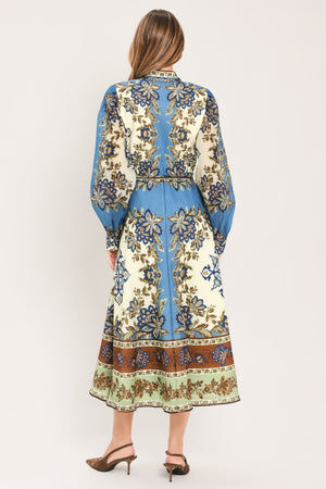A woman wearing a long-sleeved midi dress with a blue, beige, and brown floral pattern, featuring a tie waist belt | Flying Tomato