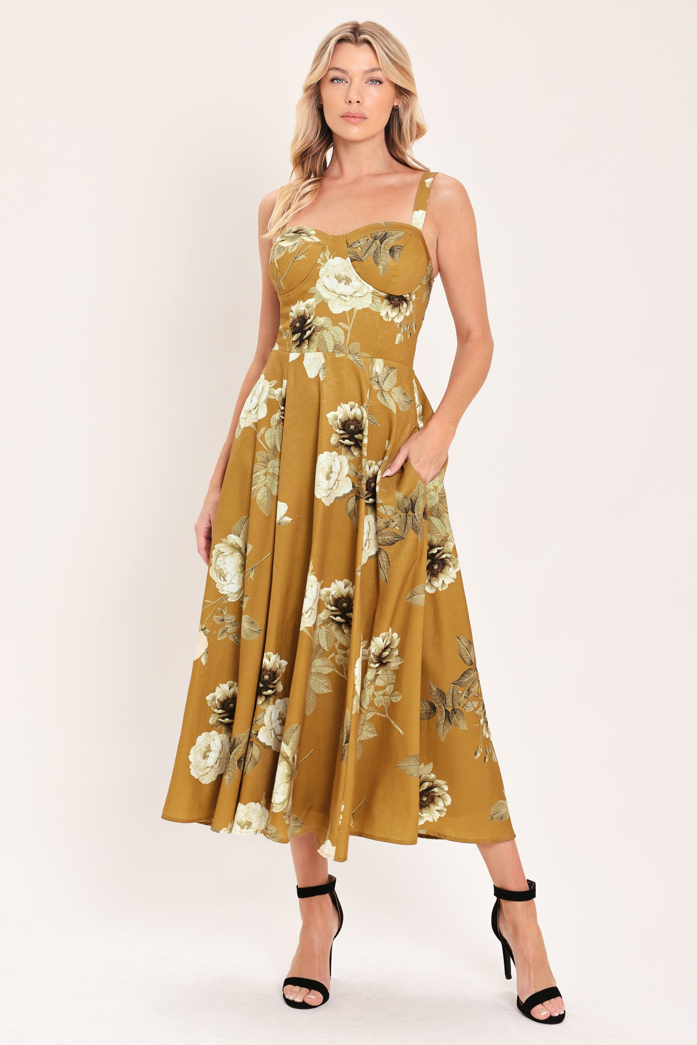 A woman modeling a sleeveless midi dress with a floral print in mustard yellow, cream, and olive green | Flying Tomato