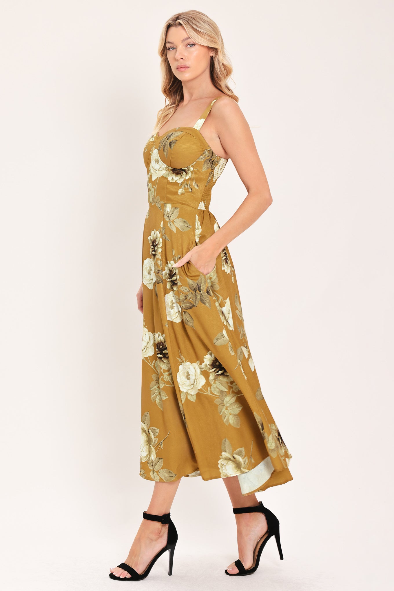 A woman modeling a sleeveless midi dress with a floral print in mustard yellow, cream, and olive green | Flying Tomato
