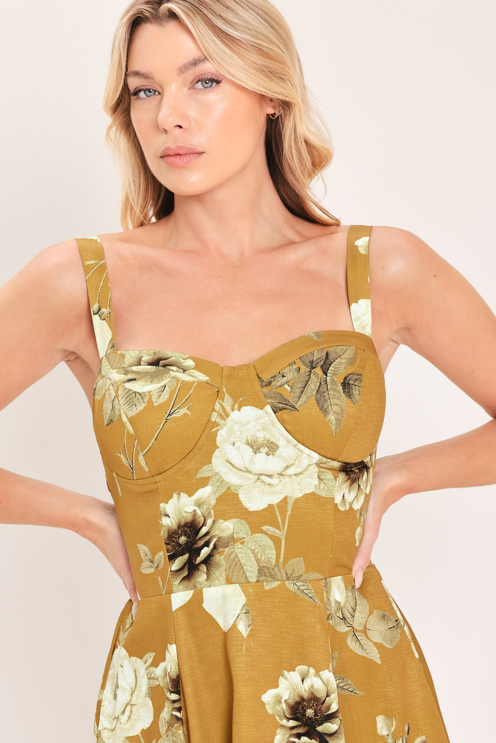 A woman modeling a sleeveless midi dress with a floral print in mustard yellow, cream, and olive green | Flying Tomato