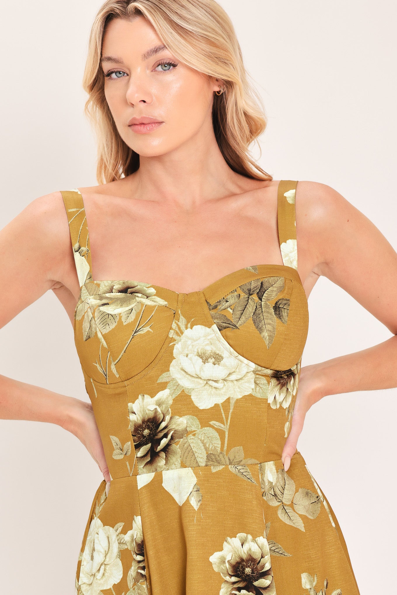 A woman modeling a sleeveless midi dress with a floral print in mustard yellow, cream, and olive green | Flying Tomato