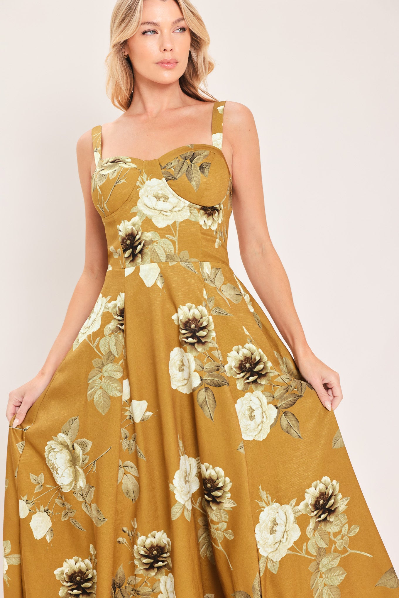 A woman modeling a sleeveless midi dress with a floral print in mustard yellow, cream, and olive green | Flying Tomato