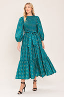 A woman wearing a teal green midi dress with a white geometric pattern, featuring balloon sleeves, a smocked bodice, and a matching waist tie | Flying Tomato