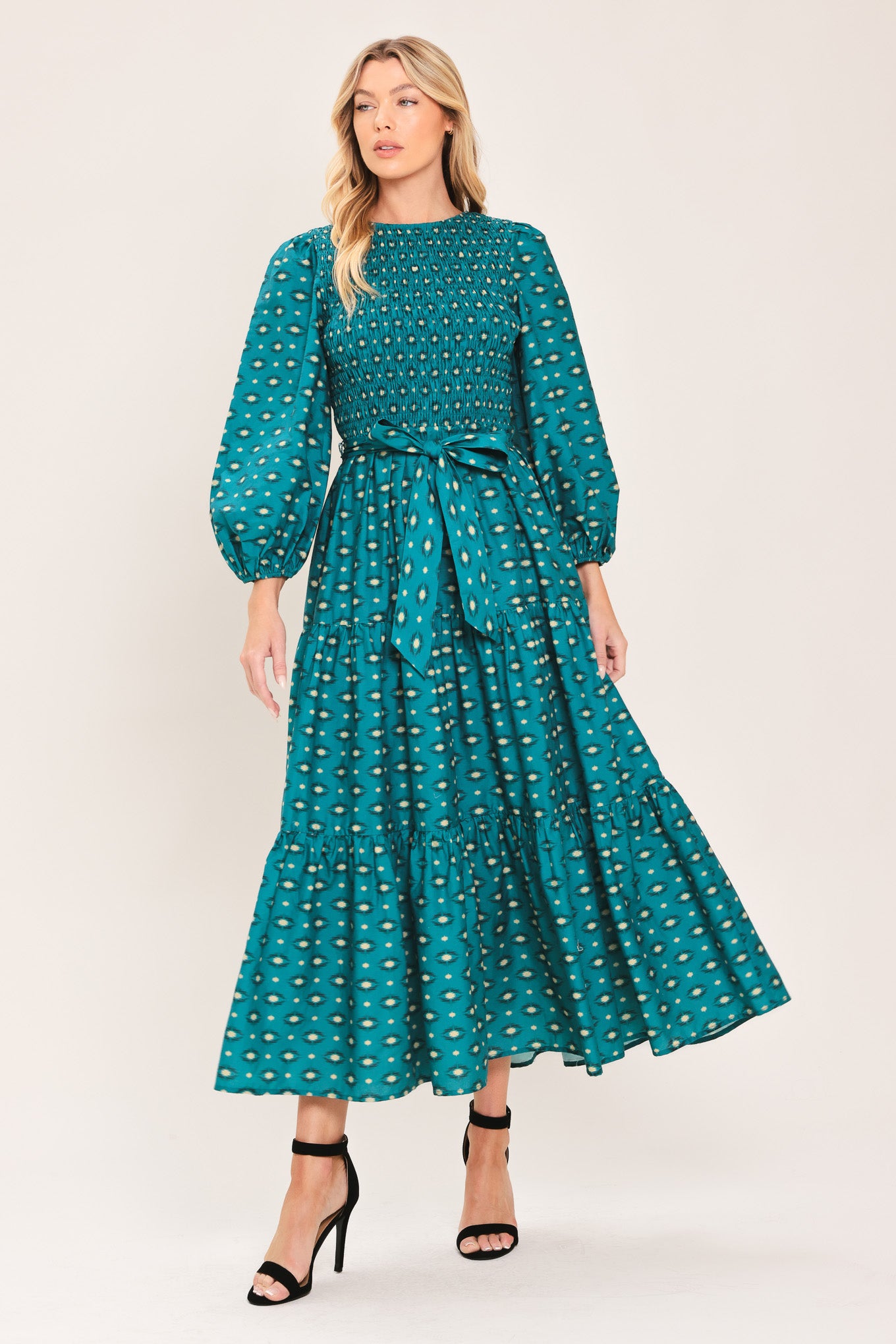A woman wearing a teal green midi dress with a white geometric pattern, featuring balloon sleeves, a smocked bodice, and a matching waist tie | Flying Tomato