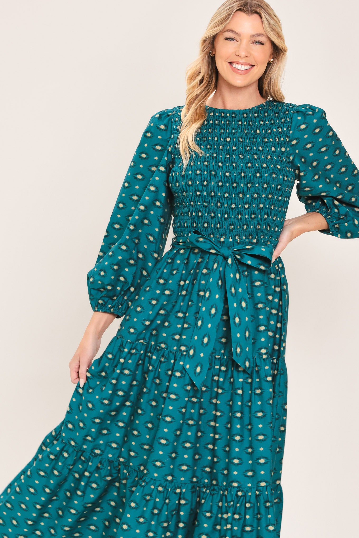A woman wearing a teal green midi dress with a white geometric pattern, featuring balloon sleeves, a smocked bodice, and a matching waist tie | Flying Tomato