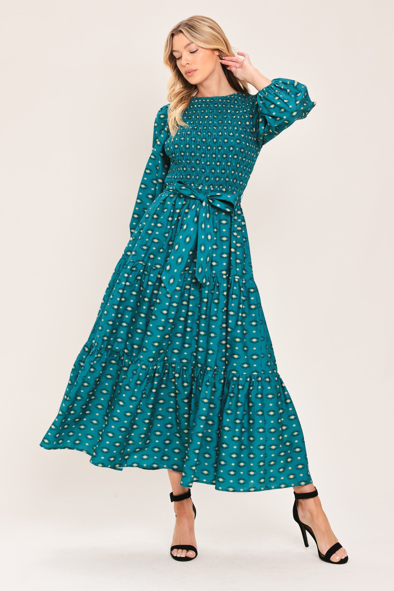 A woman wearing a teal green midi dress with a white geometric pattern, featuring balloon sleeves, a smocked bodice, and a matching waist tie | Flying Tomato
