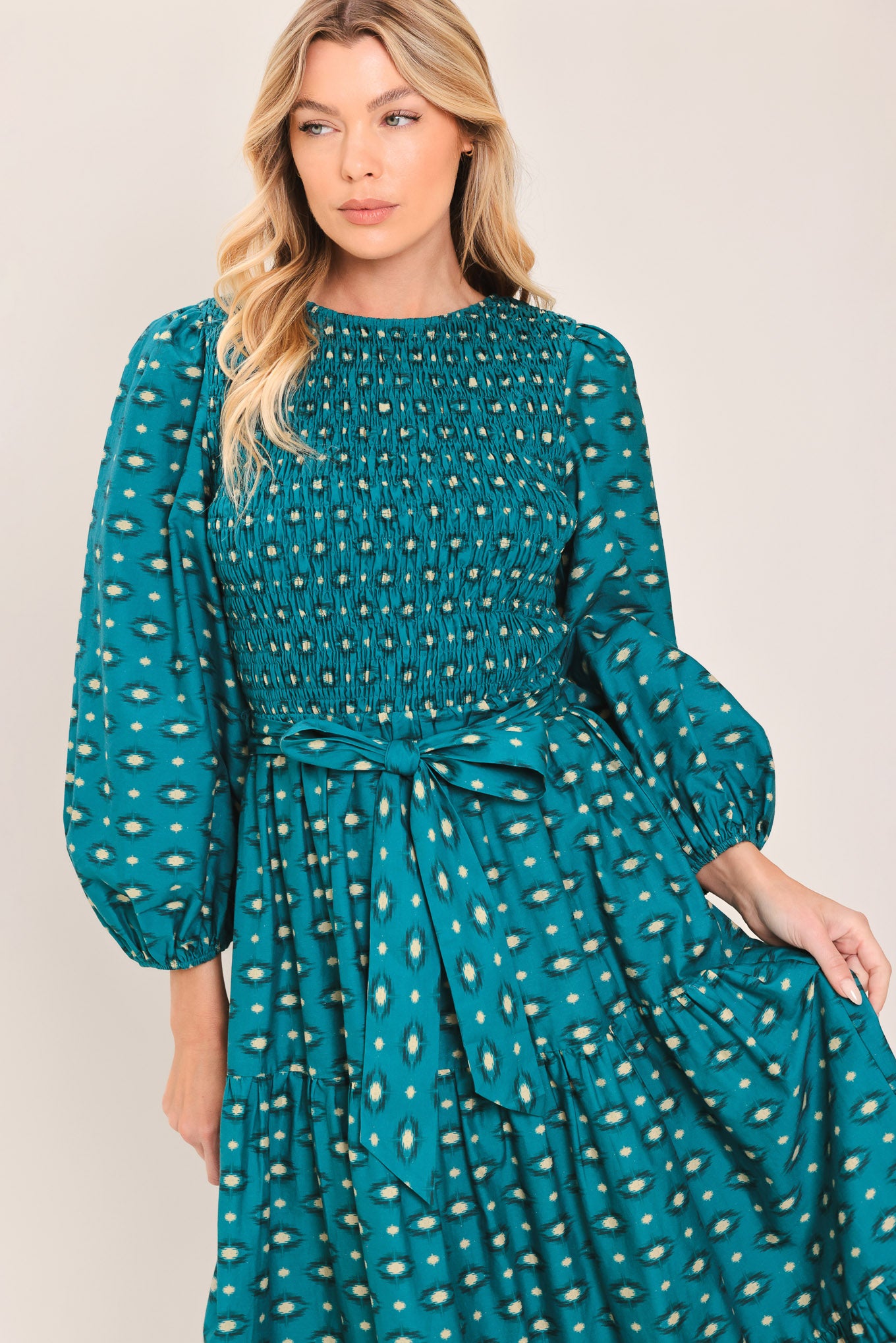 A woman wearing a teal green midi dress with a white geometric pattern, featuring balloon sleeves, a smocked bodice, and a matching waist tie | Flying Tomato