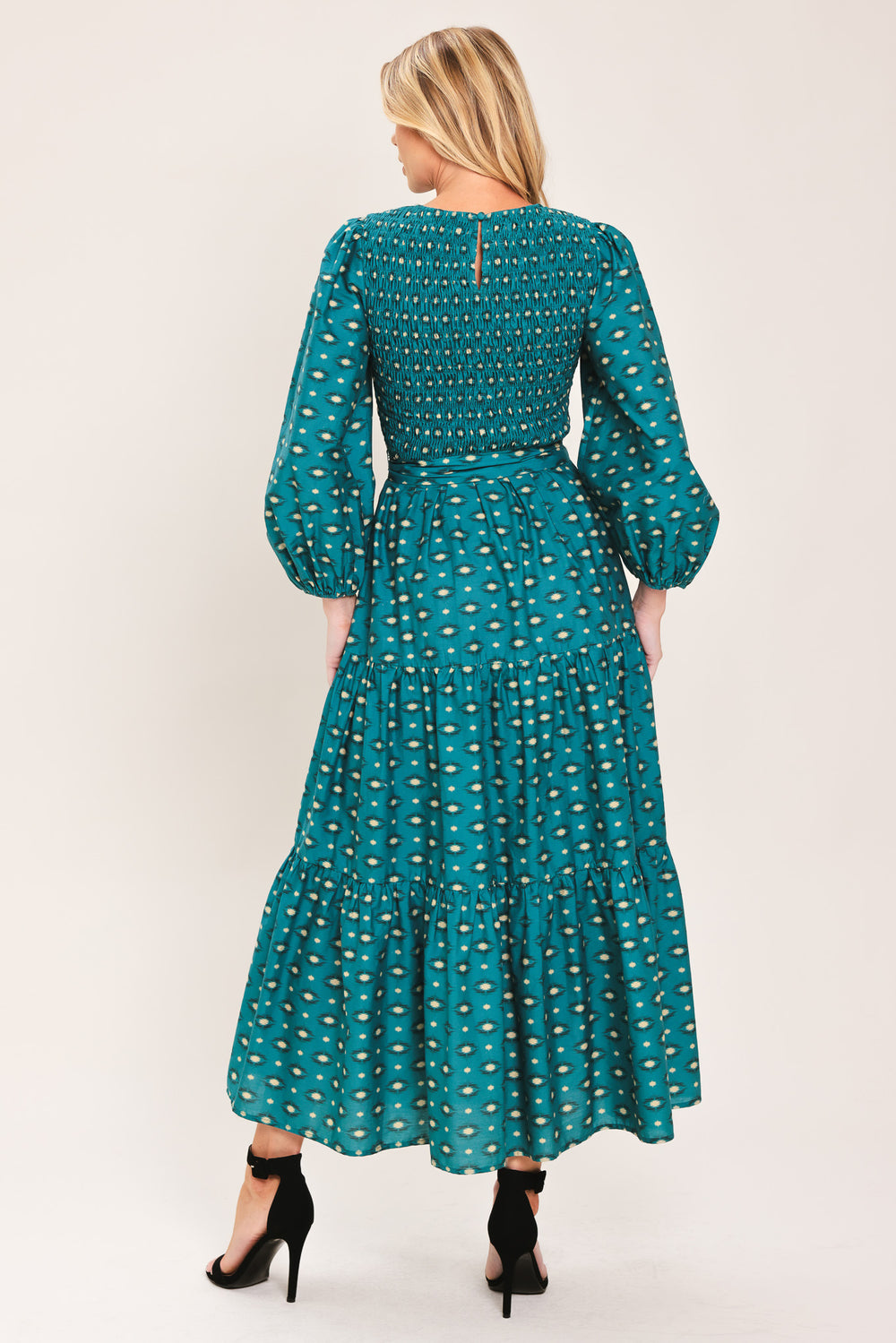 A woman wearing a teal green midi dress with a white geometric pattern, featuring balloon sleeves, a smocked bodice, and a matching waist tie | Flying Tomato