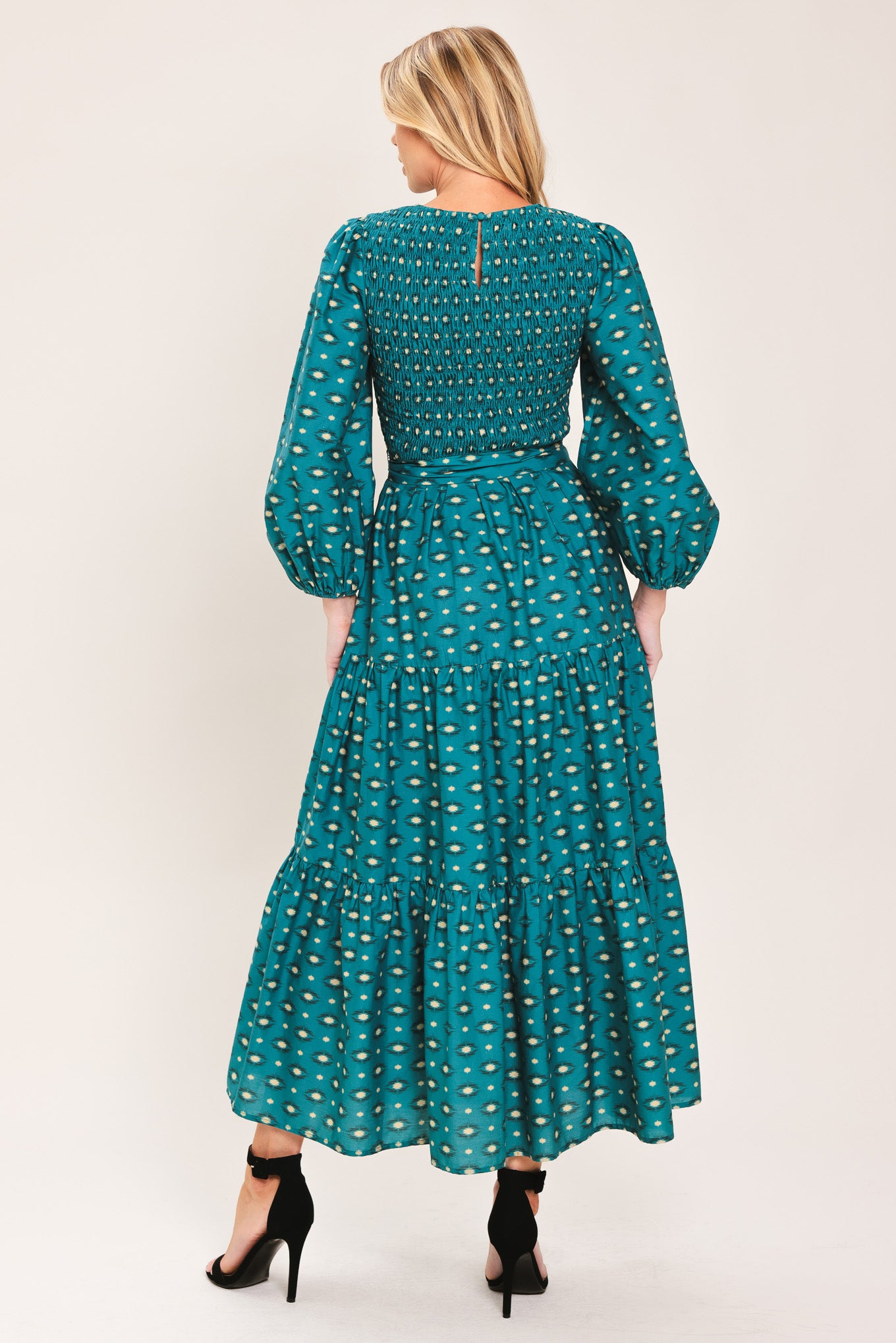 A woman wearing a teal green midi dress with a white geometric pattern, featuring balloon sleeves, a smocked bodice, and a matching waist tie | Flying Tomato