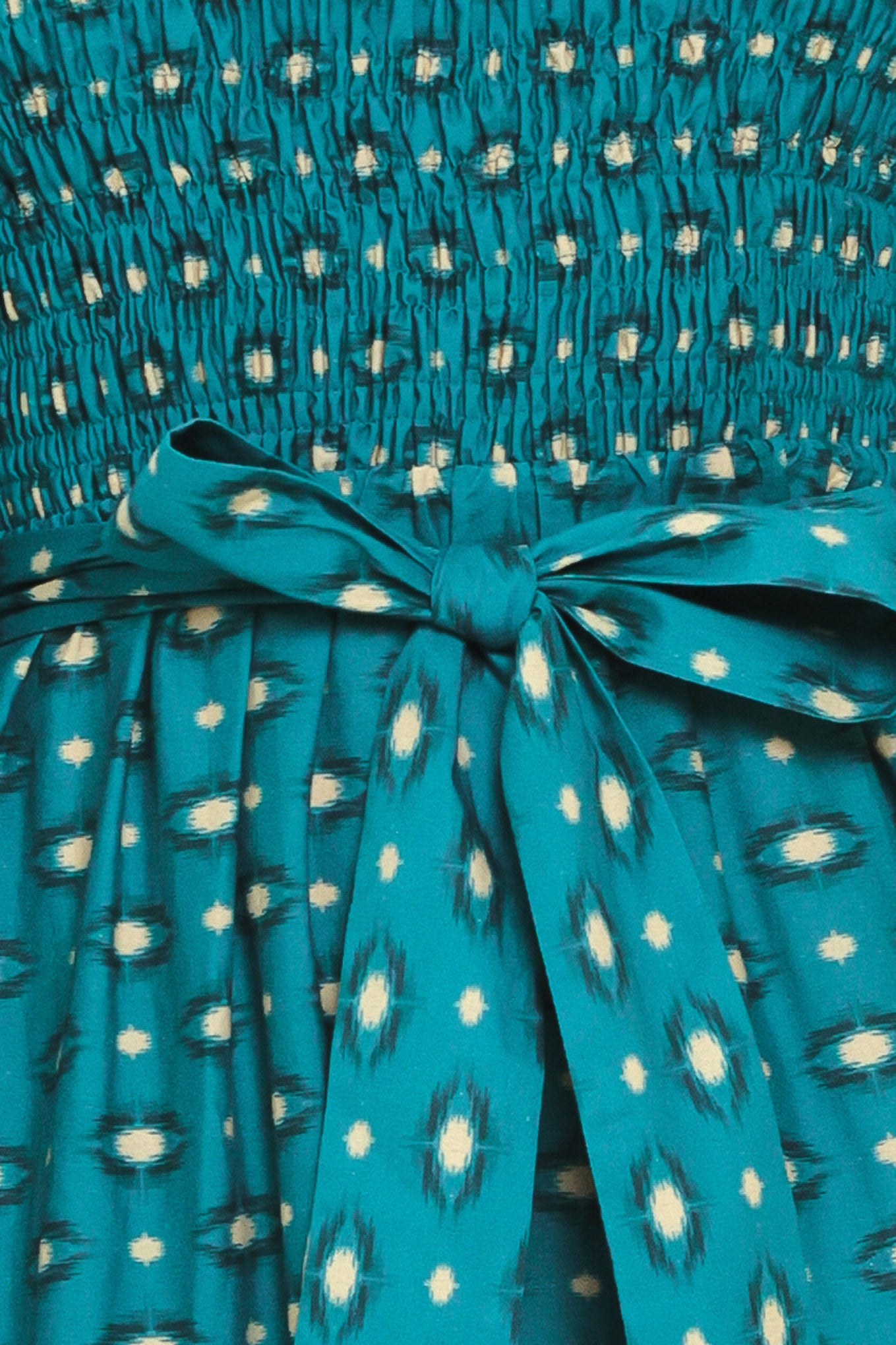 A woman wearing a teal green midi dress with a white geometric pattern, featuring balloon sleeves, a smocked bodice, and a matching waist tie | Flying Tomato