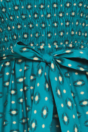 A woman wearing a teal green midi dress with a white geometric pattern, featuring balloon sleeves, a smocked bodice, and a matching waist tie | Flying Tomato
