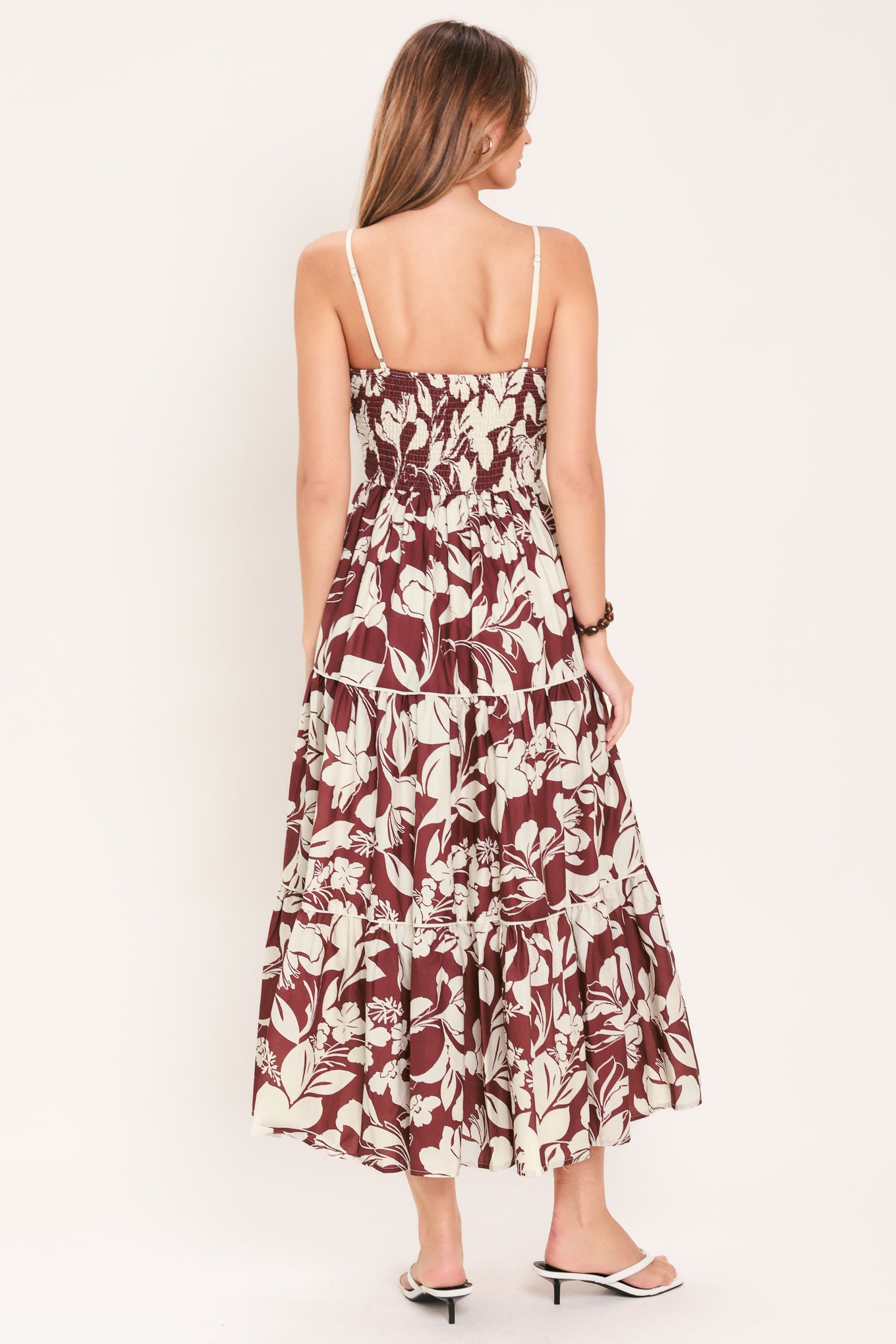 Woman wearing a floral maroon midi dress featuring cami top, waist yoke, tier skirt and smocked back bodice | Flying Tomato