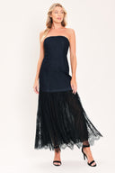 A woman modeling a strapless dark blue maxi dress with a fitted denim-like bodice and a flowing sheer tulle skirt with lace trim | Flying Tomato