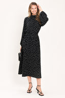 A woman modeling a black midi dress with a white polka dot pattern, featuring long balloon sleeves and a high mock neck | Flying Tomato