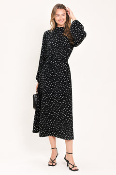 A woman modeling a black midi dress with a white polka dot pattern, featuring long balloon sleeves and a high mock neck | Flying Tomato