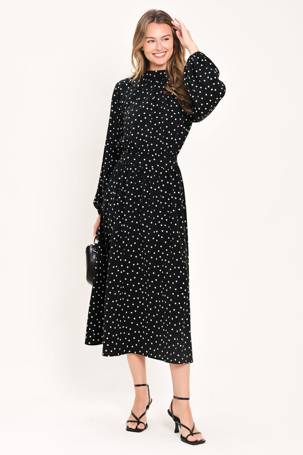 A woman modeling a black midi dress with a white polka dot pattern, featuring long balloon sleeves and a high mock neck | Flying Tomato