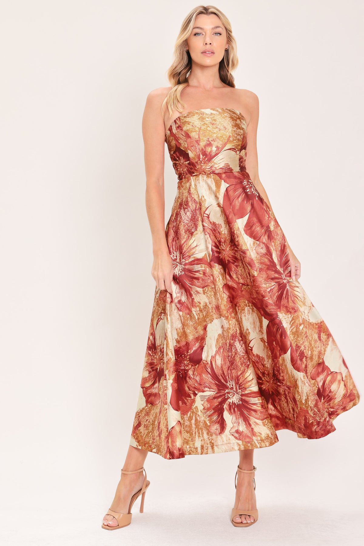 A woman modeling a strapless midi dress with a large floral print in warm rust red, gold, and beige tones | Flying Tomato