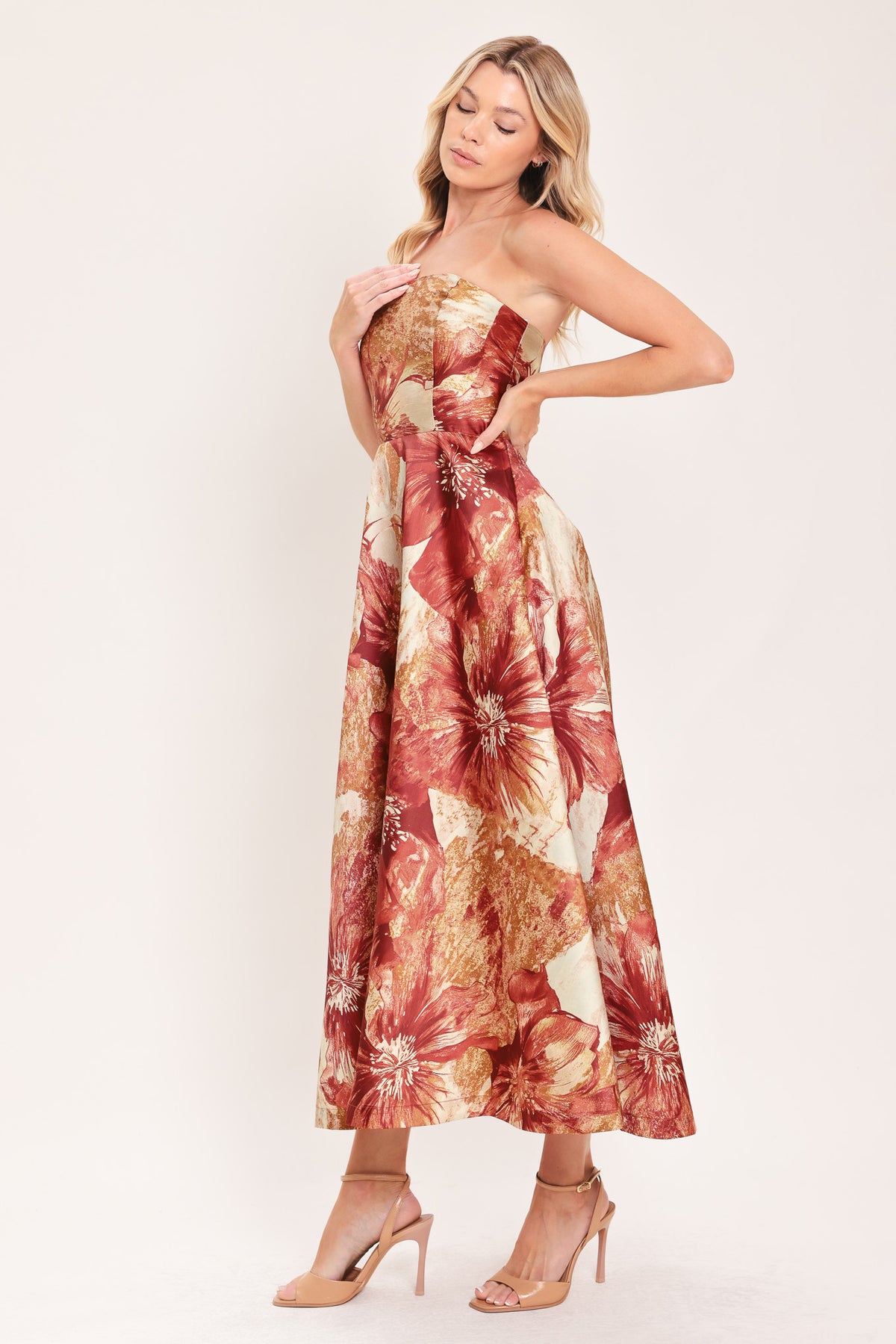 A woman modeling a strapless midi dress with a large floral print in warm rust red, gold, and beige tones | Flying Tomato