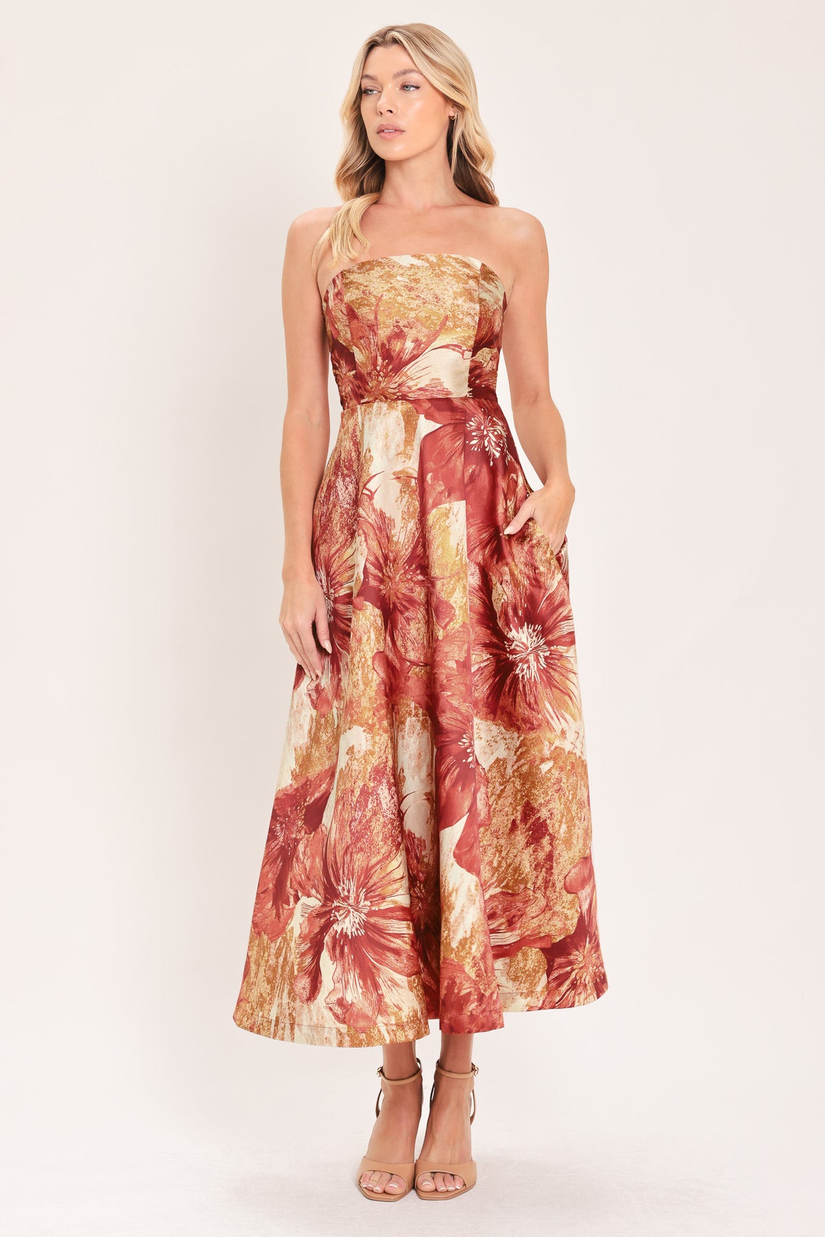 A woman modeling a strapless midi dress with a large floral print in warm rust red, gold, and beige tones | Flying Tomato
