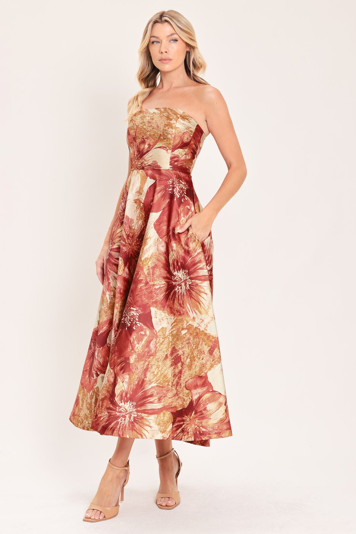 A woman modeling a strapless midi dress with a large floral print in warm rust red, gold, and beige tones | Flying Tomato