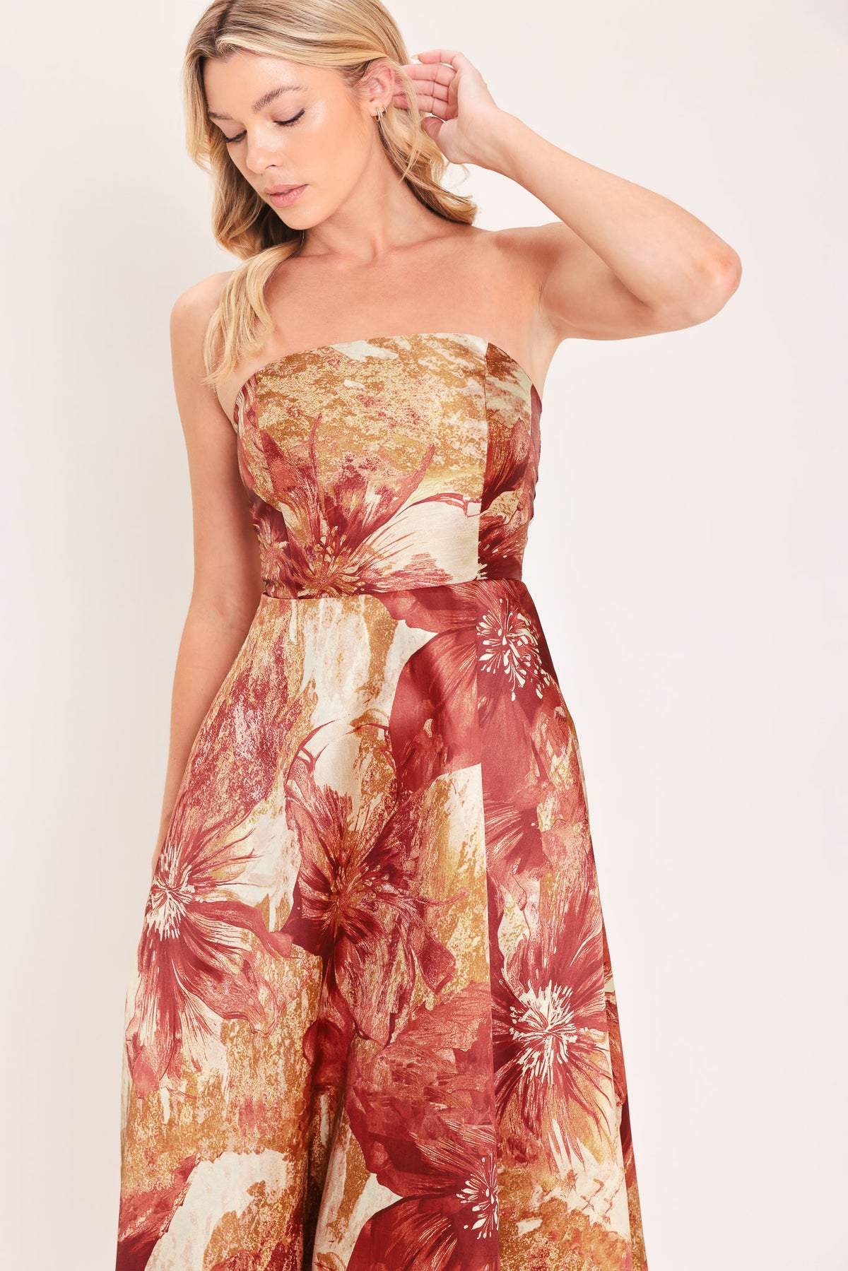 A woman modeling a strapless midi dress with a large floral print in warm rust red, gold, and beige tones | Flying Tomato