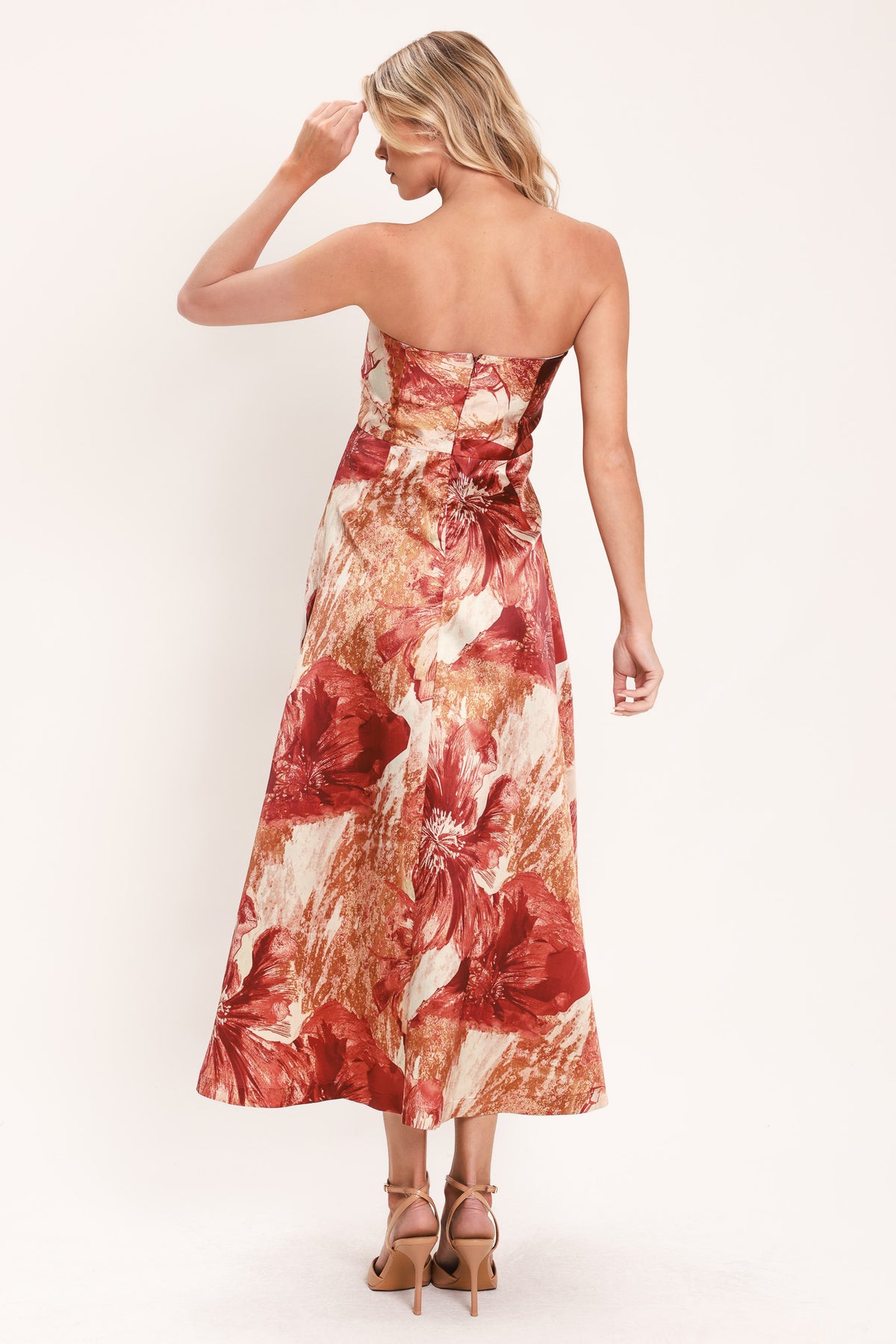 A woman modeling a strapless midi dress with a large floral print in warm rust red, gold, and beige tones | Flying Tomato