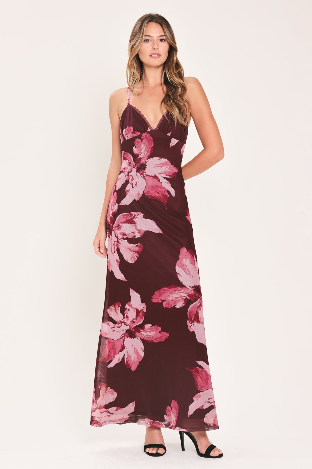 A woman modeling a sleeveless maxi dress with a dark burgundy base and large pink floral print | Flying Tomato