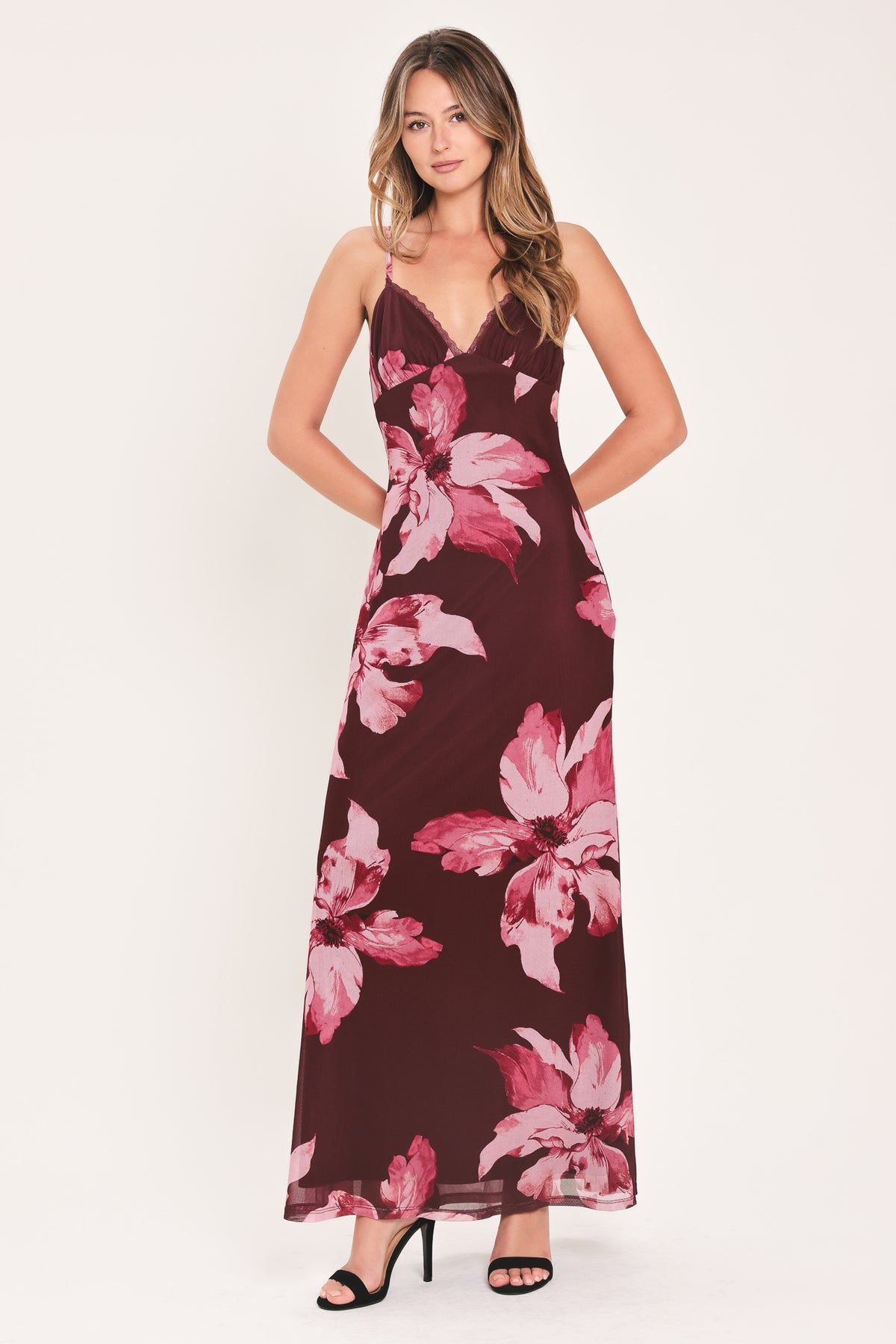 A woman modeling a sleeveless maxi dress with a dark burgundy base and large pink floral print | Flying Tomato
