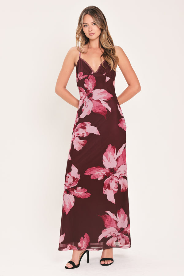 A woman modeling a sleeveless maxi dress with a dark burgundy base and large pink floral print | Flying Tomato