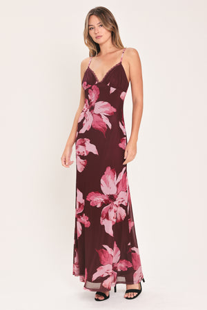 A woman modeling a sleeveless maxi dress with a dark burgundy base and large pink floral print | Flying Tomato